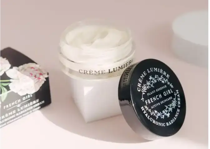 A sleek black-lidded jar of french girl crème lumière hyaluronic radiance cream, featuring elegant white lettering and a delicate floral design on the lid.